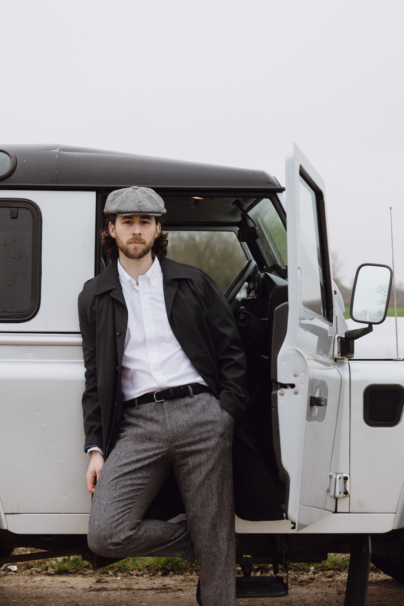 A man leaning on a Land Rover and wearing a Christys’ 8 Piece Baker Boy Tweed Cap
