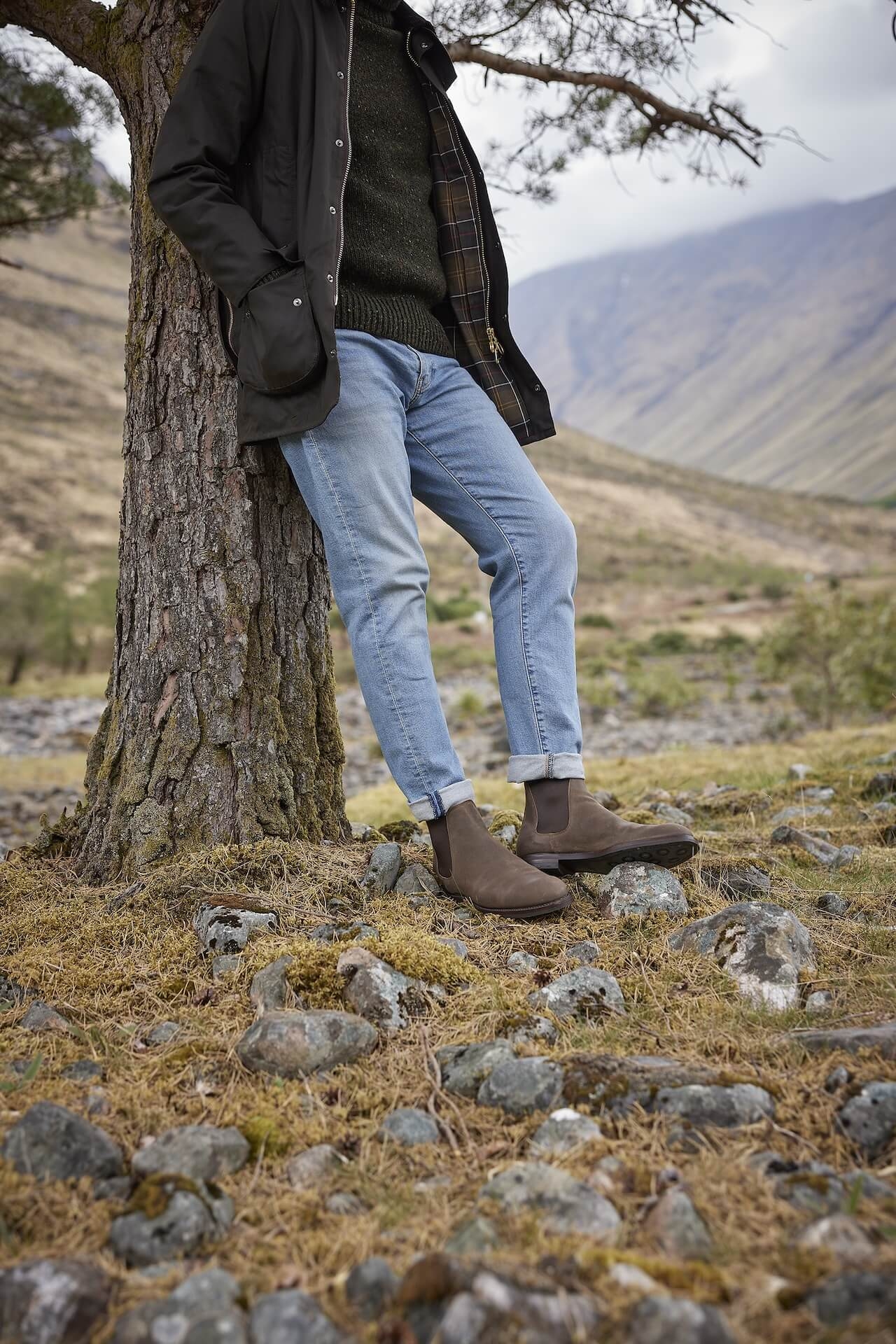 A man wearing Crockett & Jones boots leaning against a tree