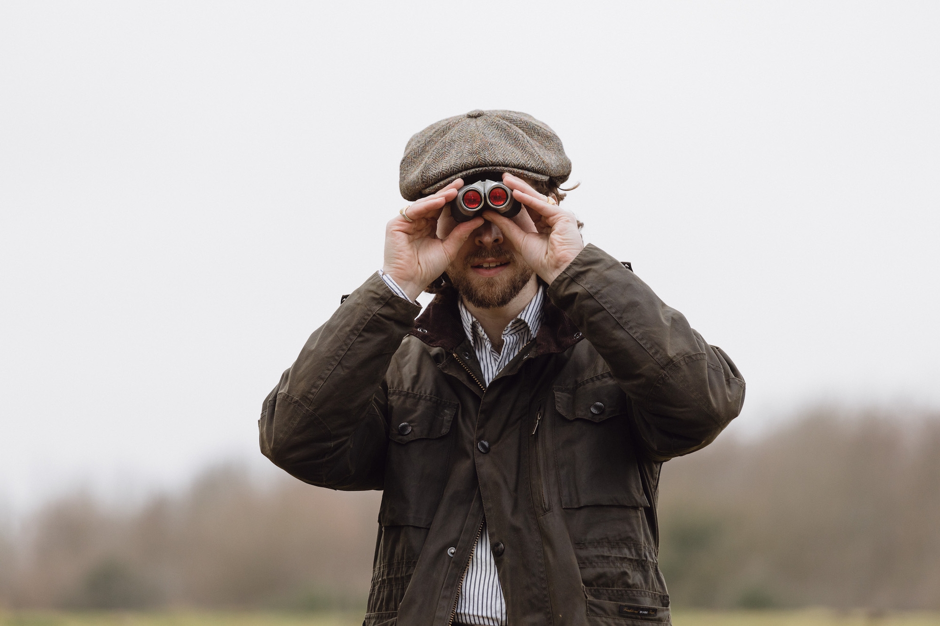 A man wearing a Christys’ Baker Boy Tweed Cap looking through binoculars