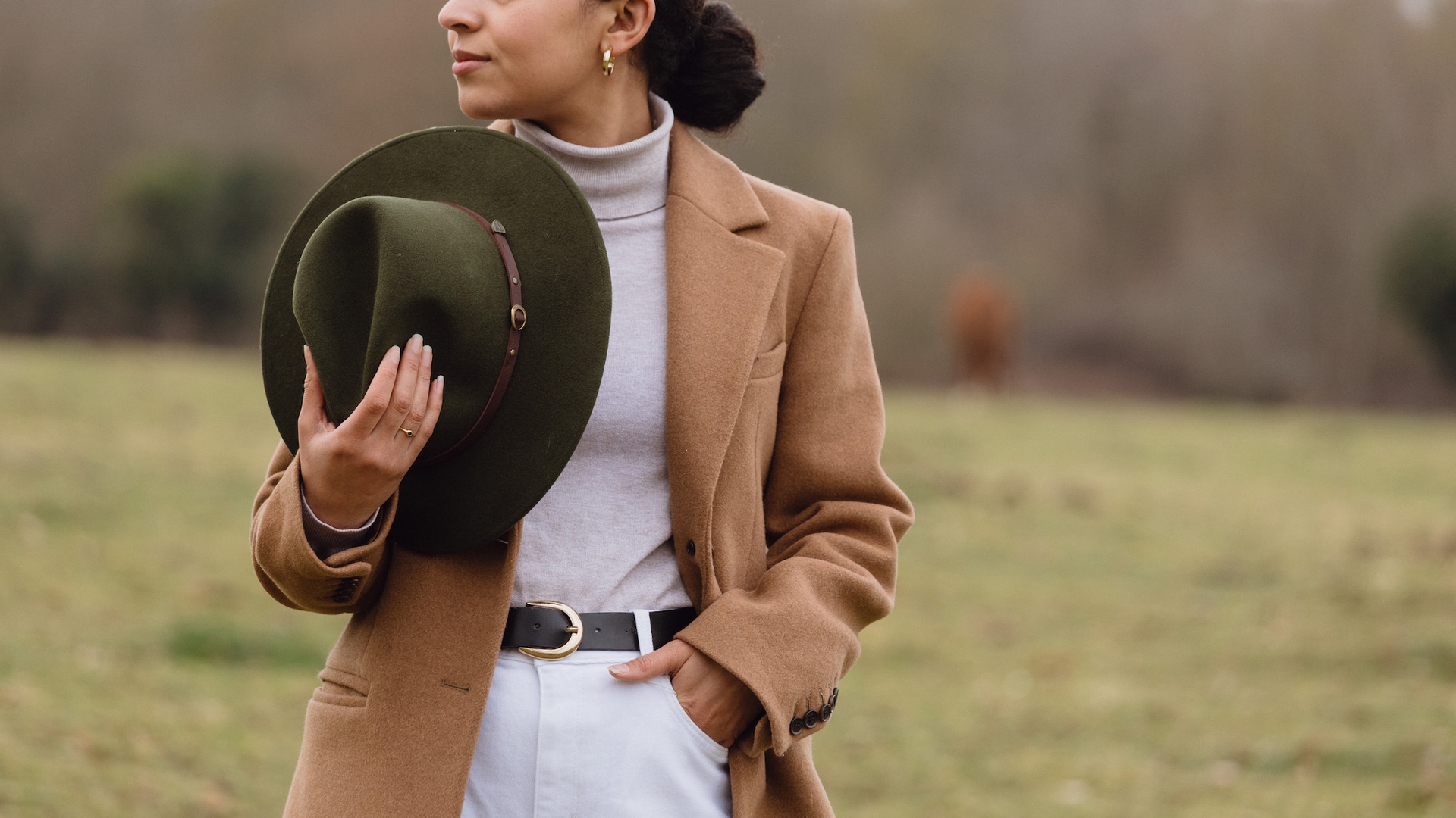 A woman in a field holding a brgreenown Christys’ fedora